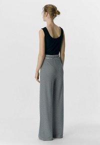 Top in un tessuto a costine nero abbinato a pantaloni a vita alta e gamba larga con strisce orizzontali blu navy e bianche. Vista posteriore mostrata.