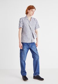 Stripet skjorte med korte ermer i blått og hvitt, kombinert med blå cargo-jeans med flere lommer, og svarte sneakers.