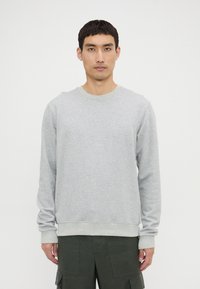 Grey cotton sweatshirt with a ribbed crew neck and cuffs, featuring a relaxed fit and smooth texture. Worn over dark cargo pants.