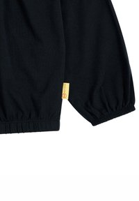Schwarzes Langarmoberteil aus weichem Baumwollstoff. Mit elastischen Bündchen und einem kleinen gelben Etikett mit Branding an der Seite.