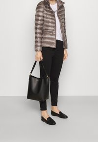 Grå puffjacka, vit T-shirt, svarta jeans, svarta loafers, håller en svart läderbucketbag med gyllene detaljer.