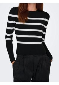 Haut à manches longues rayé noir et blanc en tricot côtelé, avec un col rond et une silhouette ajustée. Porté avec un pantalon rayé à taille haute.