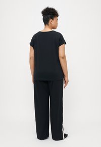 Sort kortærmet top med en afslappet pasform, parret med sorte brede bukser med hvide sidestutter. Glat tekstur, simpelt design.