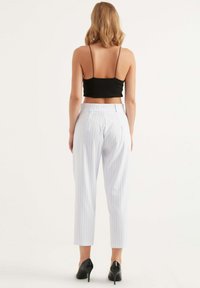 Zwart getailleerd crop top gecombineerd met witte pinstriped broeken, met een hoge taille en taps toelopende pijpen. Gestyled met zwarte hakken.