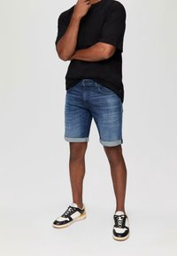 Shorts di denim blu chiaro con risvolti, abbinati a una maglietta nera e scarpe da ginnastica nere con dettagli bianchi e gialli.