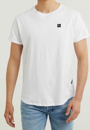 Hombre vistiendo una camiseta blanca de manga corta sin estampado con un pequeño logotipo negro en el lado izquierdo del pecho y jeans de color azul claro.