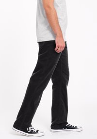 Pantalon en velours côtelé noir à coupe droite et texture douce, associé à des baskets noires avec semelles en caoutchouc blanc.