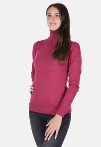 Maglione a collo alto aderente di un intenso rosa, maglia liscia, polsini e orlo a coste, con dettagli sulle spalle. Abbinato a jeans scuri.