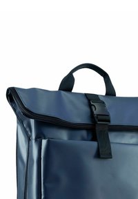 Mochila impermeable de color azul marino con una textura suave, cierre de cremallera y un asa superior. Presenta una hebilla de plástico y un diseño de solapa.