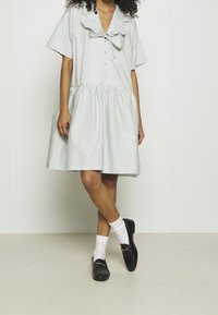 Robe courte à manches courtes à rayures vert menthe, présentée avec un col froncé, une fermeture à bouton et une jupe froncée. Associée à des mocassins noirs et des chaussettes blanches.