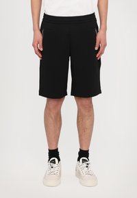Pantaloni corti neri realizzati in tessuto morbido, con una vita elastica, due tasche laterali e un design che arriva all'altezza del ginocchio. Accenti bianchi lungo le cuciture.