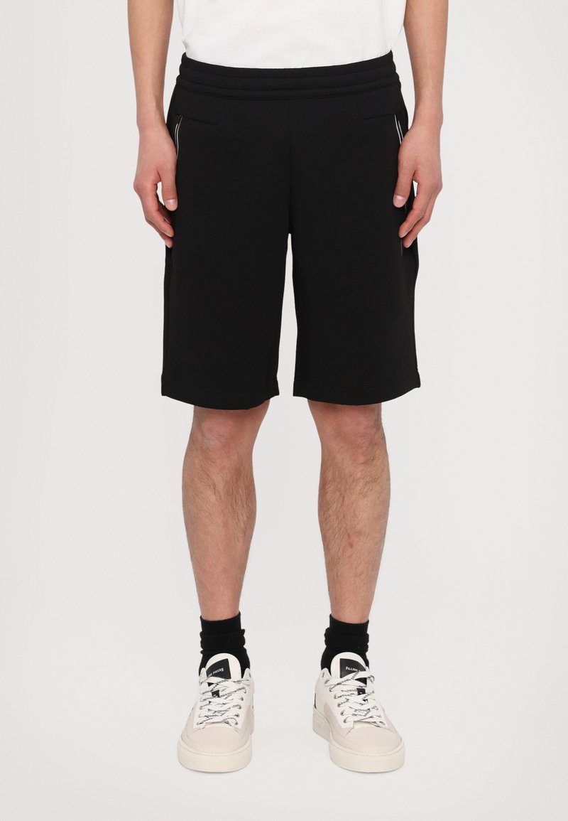 Pantaloni corti neri realizzati in tessuto morbido, con una vita elastica, due tasche laterali e un design che arriva all'altezza del ginocchio. Accenti bianchi lungo le cuciture.