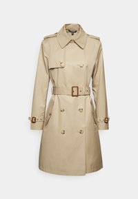 Beige trenchcoat med dubbelknäppt design, stora knappar, axelklaffar, sidofickor och midjebälte. Slät tygtextur.
