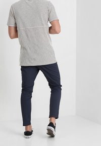 Męska koszulka w paski w jasnobeżowy i ciemnoniebieski wzór, zestawiona z dopasowanymi ciemnoniebieskimi spodniami i czarnymi tenisówkami.