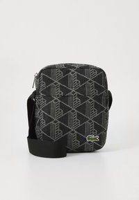 Crna torba na rame od tkanine s geometrijskim uzorkom, sivim detaljima, zatvaranjem na patentni zatvarač i zelenim logotipom. Uključena podesiva traka.