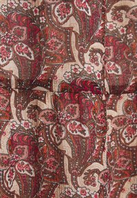 Tessuto con un motivo paisley caratterizzato da accenti rossi, rosa e marroni su uno sfondo beige. Texture stropicciata con una caduta fluida.