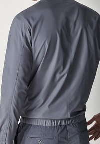 Szara lekkia kurtka o gładkiej teksturze, ze ściągaczem u dołu i prostym wzornictwem. Posiada stójkę i długie rękawy.