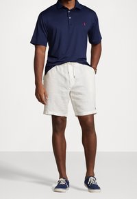 Námornícky polo tričko s červeným logom, bílé lněné šortky s elasticým pasem, modré plátěné tenisky s bílými podrážkami a šňůrkami.