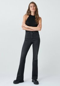 Jean noir taille haute évasés avec une coupe flatteuse, présentant un design classique à cinq poches et des coutures robustes, associé à un haut noir ajusté.