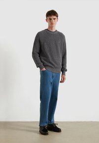 Maglione grigio a maglia strutturata con collo rotondo e polsini a coste, abbinato a jeans blu a gamba dritta e scarpe nere stringate.
