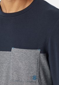 T-shirt blu navy con taschino a righe grigie. Presenta un collo rotondo e un logo ricamato in blu sulla tasca. Materiale in cotone morbido.