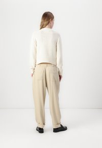 Lys beige strikket genser med ribbet kant og mansjetter, kombinert med lys beige bukser med avslappet passform, baklommer og oppbrettede bein.