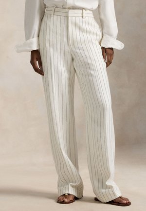 Pantalon blanc à jambes larges avec des rayures verticales bleu marine, doté d'une taille haute, d'un devant plissé et de poches latérales, associé à des sandales marron.