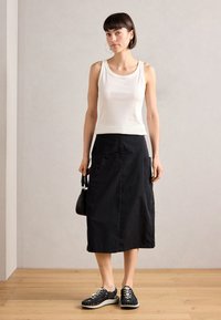 White tank top, black mid-length skirt with pockets, and black woven sneakers. Accessories: small black bag and hoop earrings.