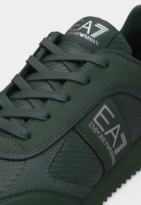 Σκούρο πράσινο αθλητικό παπούτσι EA7 Emporio Armani με ανάγλυφες και λείας υφές επιφάνειες, κορδόνια και λεπτομέρειες με λογότυπο στη γλώσσα και την πλευρά.