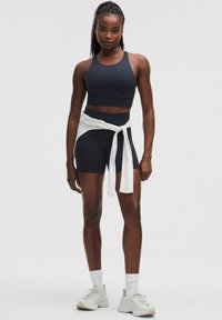 Tengerészeti sportcrop top és rövidnadrág, derékra kötött fehér inggel. Simaságot és illeszkedést biztosító dizájn, réteges textúrákkal. A megjelenést fehér sportcipők zárják le.