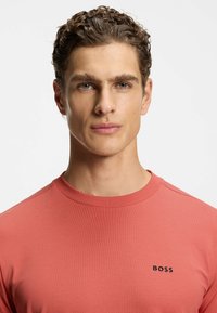 Short-sleeve coral t-shirt made of ribbed fabric, featuring a crew neckline and a black "BOSS" logo on the upper left chest.