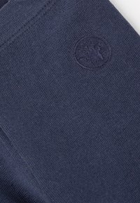 Tessuto di cotone blu navy con una texture liscia e un logo circolare in rilievo sul lato sinistro inferiore. Design semplice e privo di fronzoli.