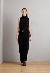 Black sleeveless turtleneck top paired with high-waisted black trousers. Notable round silver buckle on the belt. Brown lace-up shoes.