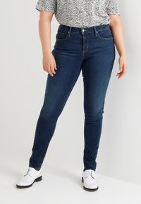 Jeans skinny azul oscuro con una textura suave, cinturilla alta y diseño clásico de cinco bolsillos, combinados con una blusa de manga corta con estampado.