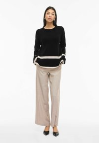 Melns adīts džemperis ar bēšām svītrām apakšmalā, kombinēts ar gaiši bēšām platām biksēm. Modelis valkā melnas, smailas augstpapēžu kurpes.