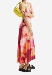 Maxi sukienka z gradientowym wzorem w odcieniach różu, czerwieni i pomarańczu. Połączona z jasnoróżową torebką na ramię i czarnymi sandałami na płaskiej podeszwie.