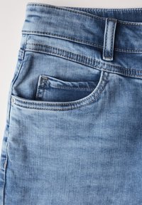 Ljusblå denimjeans med en mjuk textur, med en framficka, bälteshällor och kontrasterande sömmar längs kanterna.