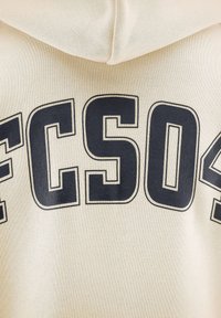 Felpa color crema con lettering nero in grassetto "FCS04" sul petto, in tessuto testurizzato e dalla forma rilassata.