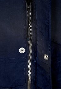 Navy blue jacket featuring a metal zipper, snap fasteners, and textured fabric with subtle stitching details.