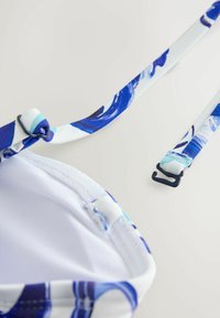 Niebieski i biały stanik bikini w kwiatowy wzór, z regulowanymi ramiączkami i zapięciem na haczyk. Tkanina ma gładką teksturę.