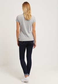 Šedé tričko s krátkým rukávem v kombinaci s tmavě modrými skinny džíny. Džíny mají světlé švy a ohrnuté manžety, doplněné bílými teniskami.