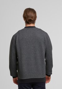 Mørk grå sweater med en tekstureret vævning, ribbede manchetter og kant samt en rund halsudskæring. Bagsiden viser et rent, enkelt design.