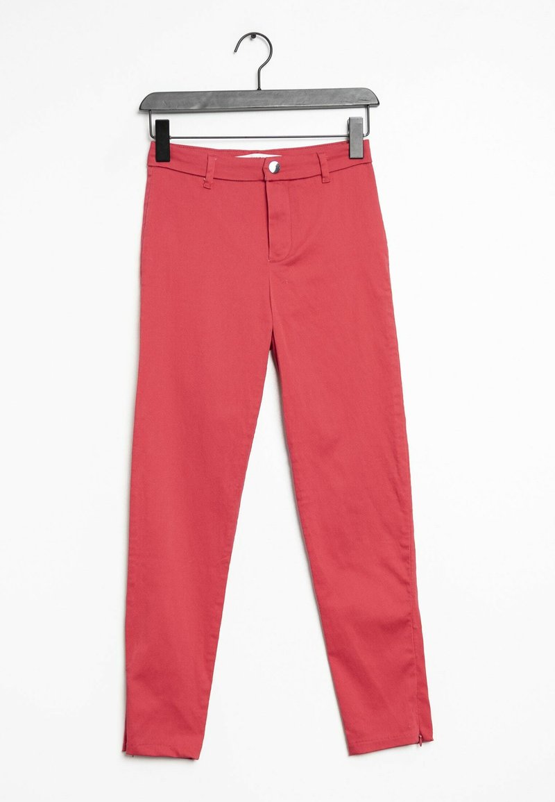 Pantalon slim en coton rouge avec fermeture à bouton, passants de ceinture et fermeture éclair aux chevilles, suspendu à un cintre noir sur fond blanc.