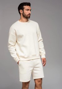 Felpa color crema e pantaloni corti realizzati in morbido cotone. La felpa presenta un collo rotondo e polsini a costine, mentre i pantaloni corti hanno una vita elastica.