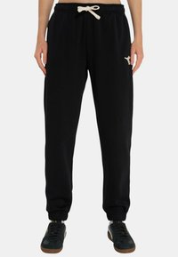 Pantaloni da jogging neri con una texture morbida, vita elastica, cordino avorio e polsini a coste. Presentano un piccolo logo sulla coscia sinistra.