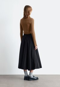 Brown ribbed long-sleeve top paired with a black, full-length skirt. Worn with gray socks and black shoes with a thick sole. Plain background.