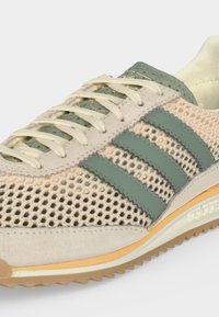 Μπεζ και ανοιχτό πράσινο αθλητικό παπούτσι Adidas με πάνω μέρος από δίχτυ, τρεις πράσινες ρίγες στο πλάι, κρεμ κορδόνια και εξωτερική σόλα χρώματος καουτσούκ.