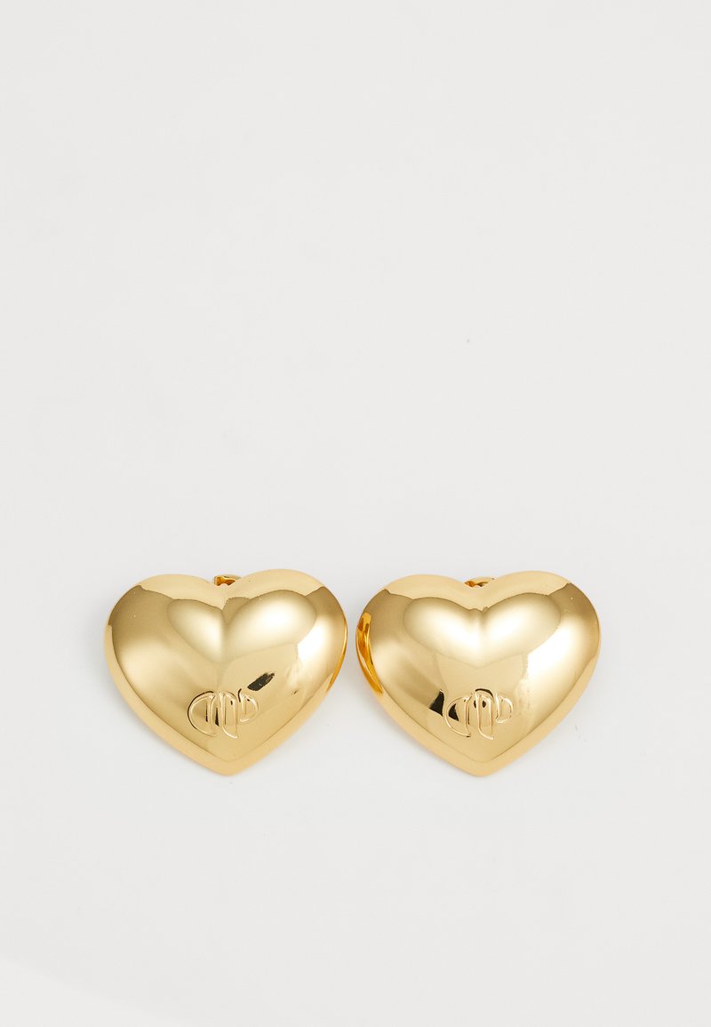 Zlaté náušnice ve tvaru srdce s lesklým, reflektujícím povrchem. Každá náušnice má na přední straně vyryté malé logo.