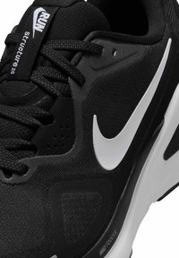 Scarpa da corsa Nike nera con una superficie testurizzata, logo bianco e una suola nera curva con un sistema di ammortizzazione visibile.