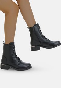 Bottines noires en simili cuir lisse, avec un laçage à l'avant, une fermeture éclair sur le côté et un petit talon empilé.